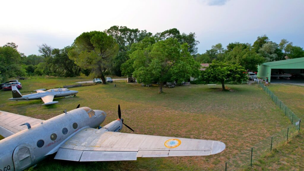 Vue d'ensemble du club-house de l'aéroclub de Valréas-Visan avec les avions anciens sur herbe